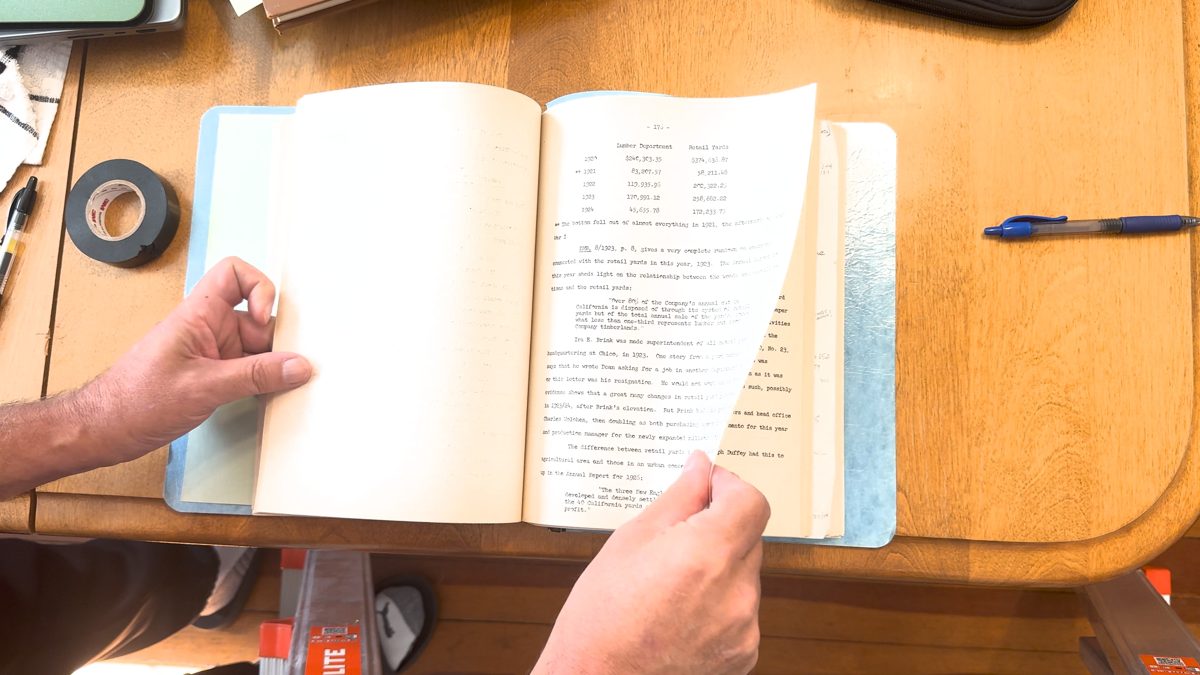 A 4K video frame looking down at a bound typescript on a desk, one hand turning a page